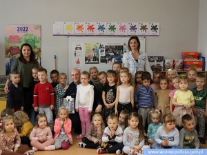 Zdjęcie przedstawia zdjęcie grupowe policjanta, przedszkolaneki i dzieci w pomieszczeniu